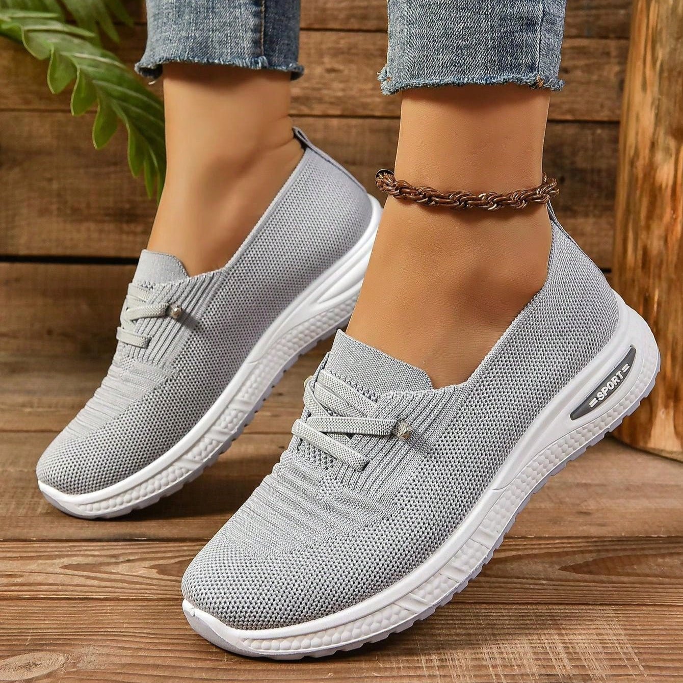 Gray sneakers worn on a wooden floor with a plant in the background