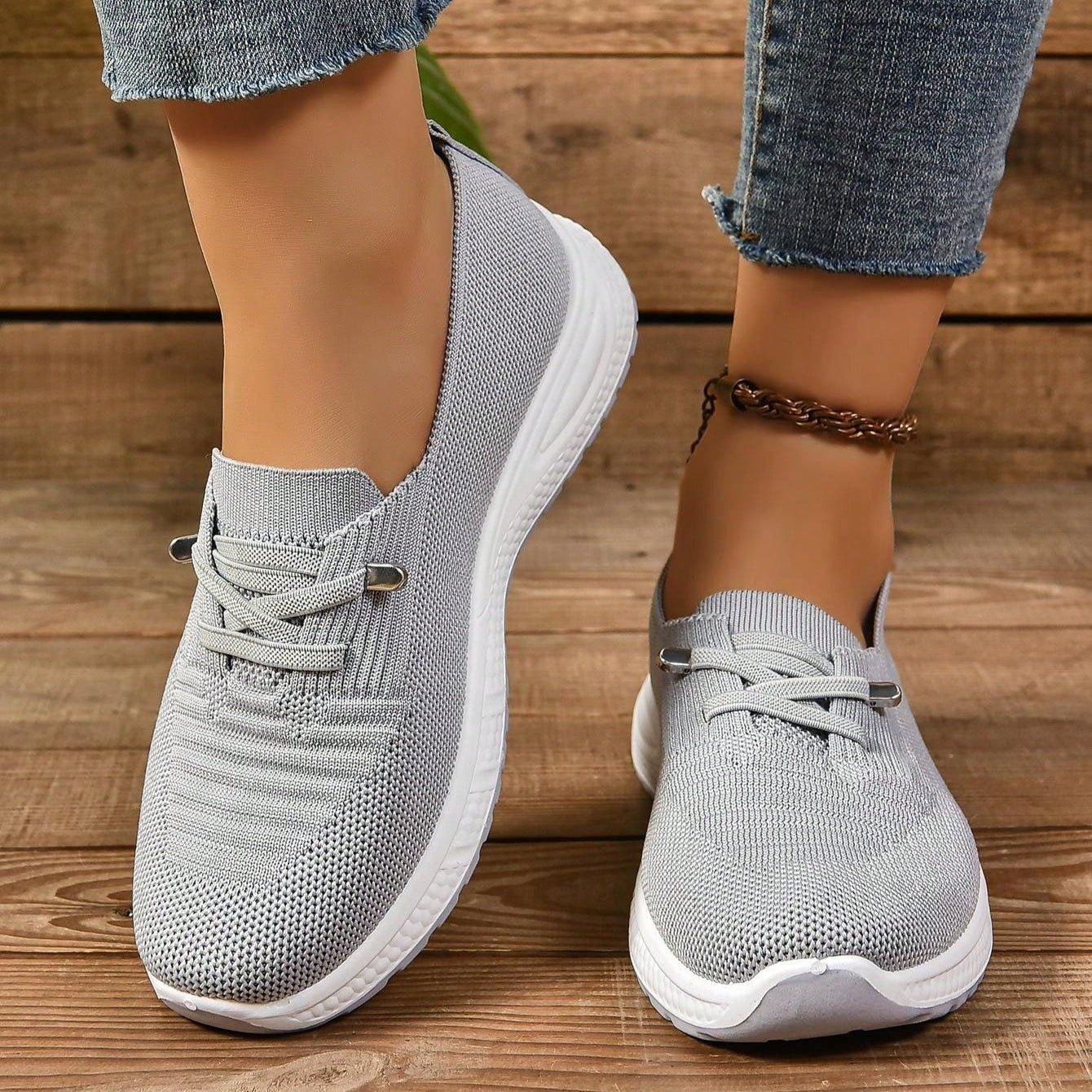 Gray sneakers with white soles worn on a wooden floor