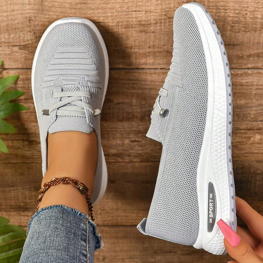 Gray sneakers being worn on a wooden floor with a plant in the corner