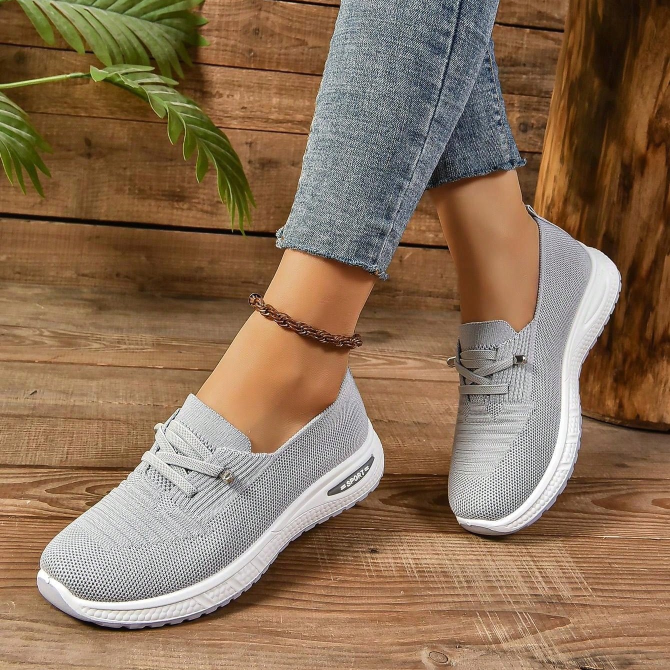 Gray sneakers worn with blue jeans on a wooden floor.