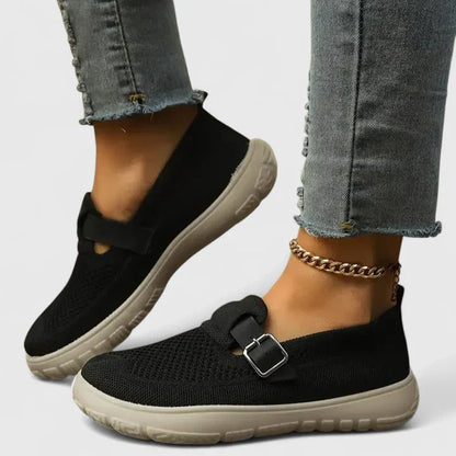 Black slip-on shoes with beige soles worn with light blue jeans on a white background