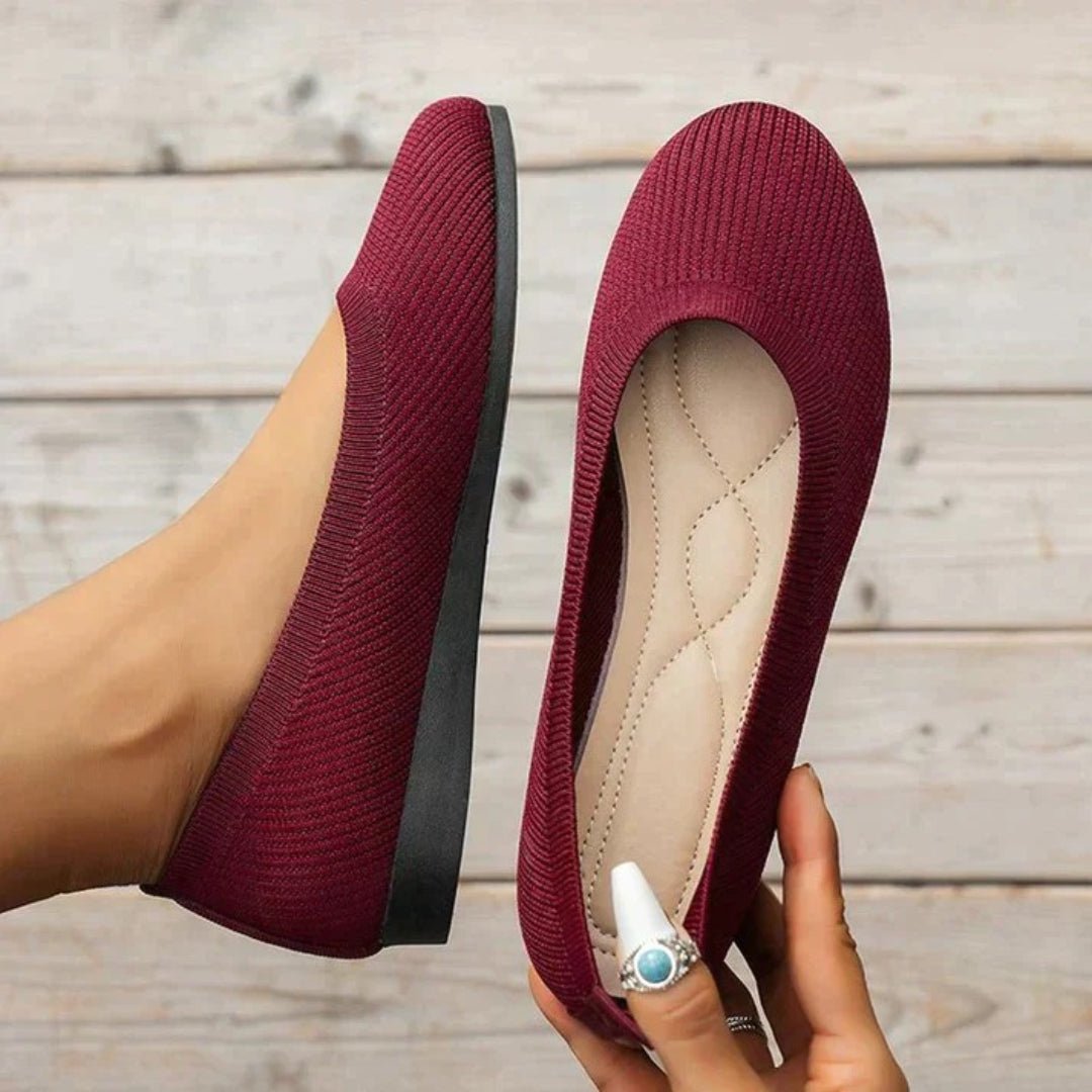 Maroon flat shoes being held up on a wooden floor