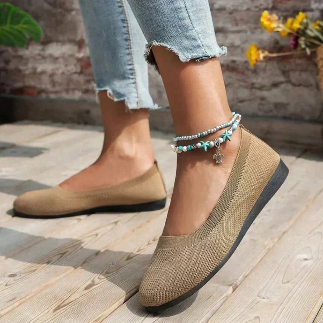 Beige flat shoes worn with light blue jeans on a wooden floor.