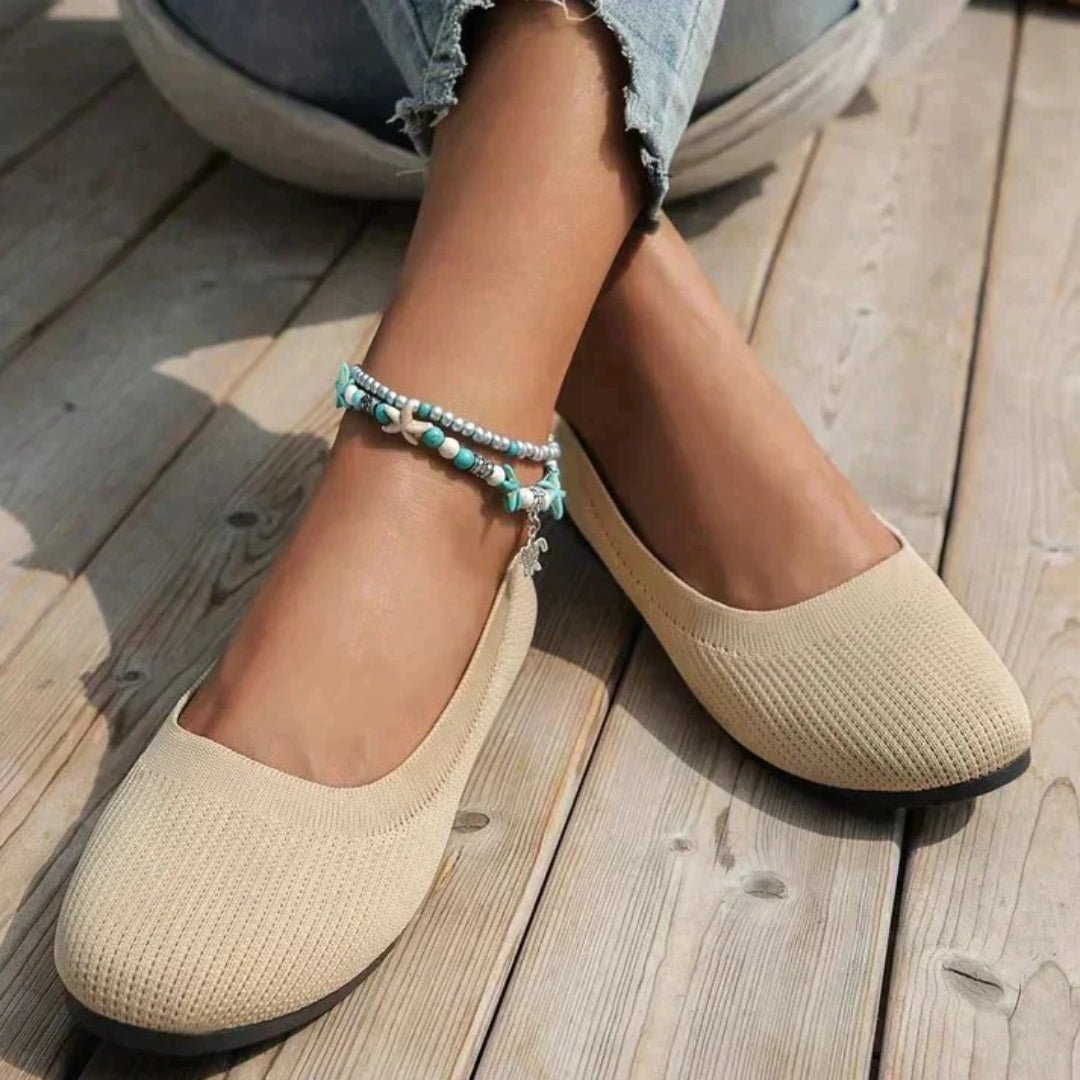 Beige flats worn on a wooden floor with a person's legs and blue jeans partially visible.