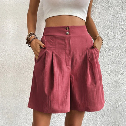 Person wearing a white crop top and pink shorts against a textured white wall.