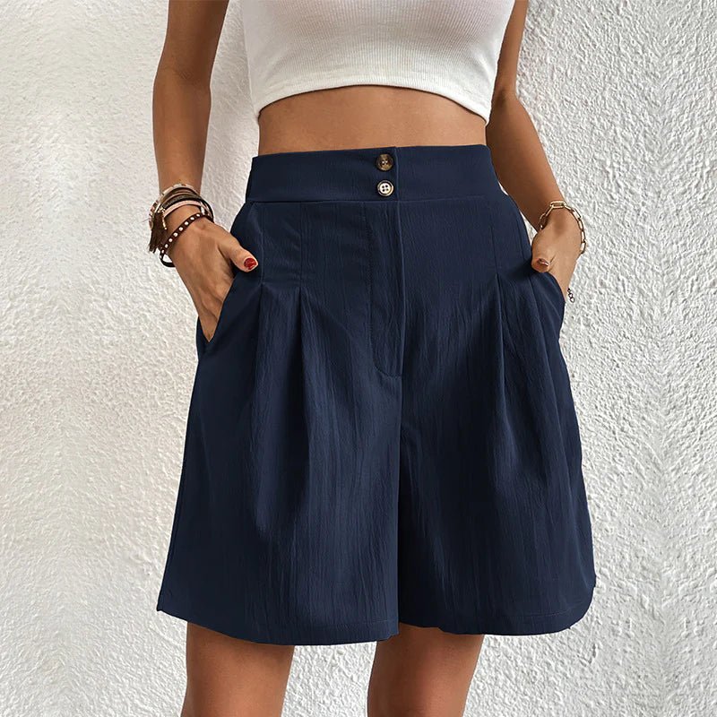 Person wearing navy shorts with a white top against a textured white wall