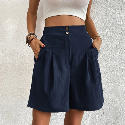 Person wearing navy shorts with a white top against a textured white wall