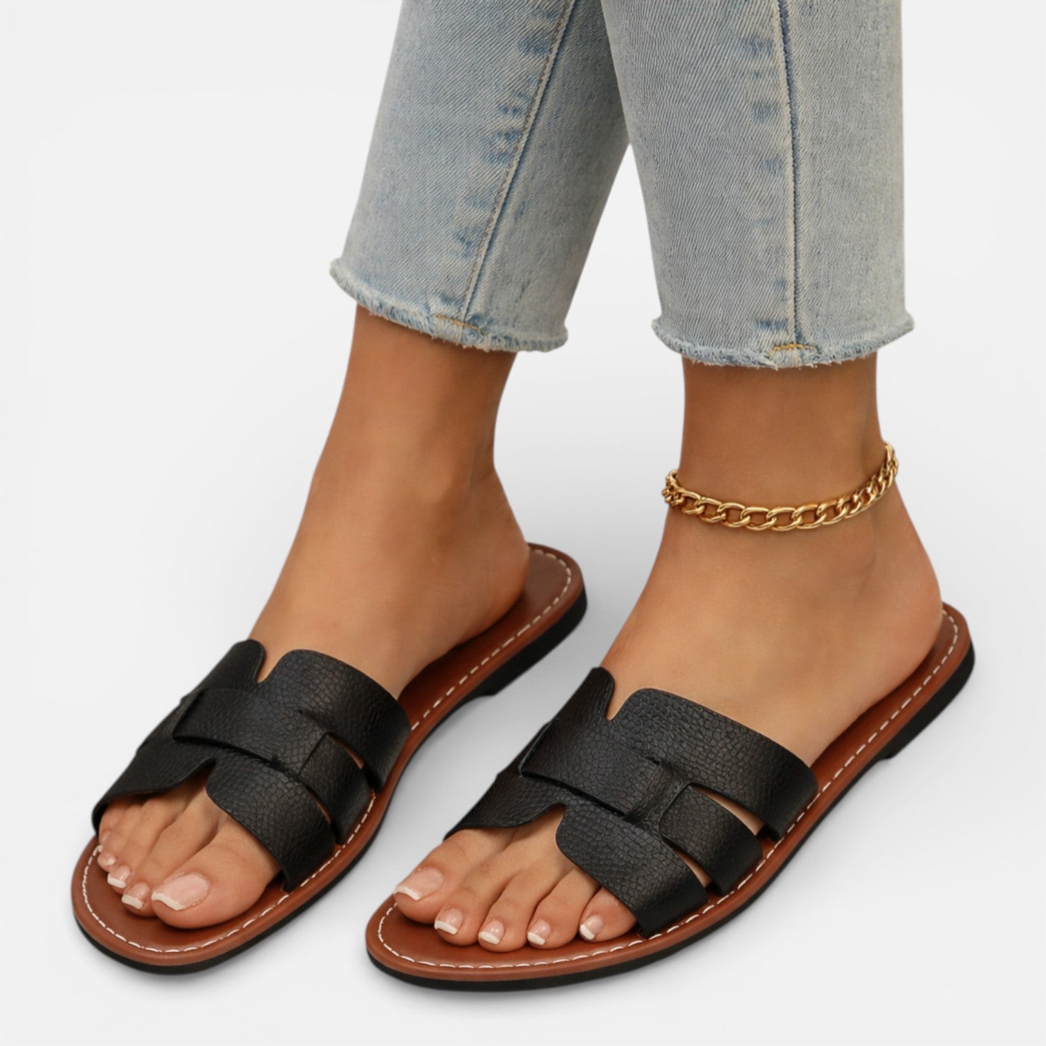 Black sandals worn with light blue jeans on a white background
