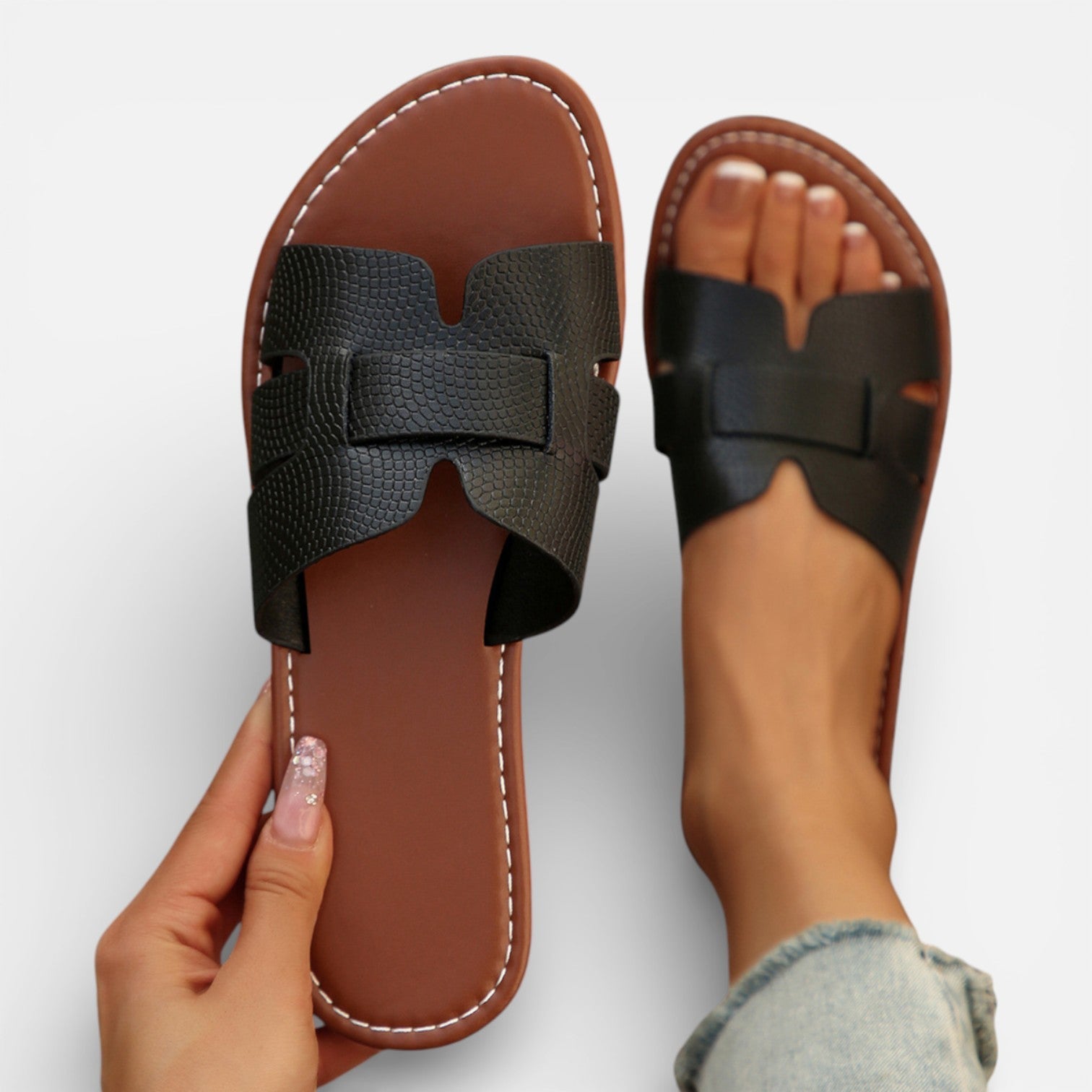 Pair of brown sandals with black straps held by a hand on a light gray background