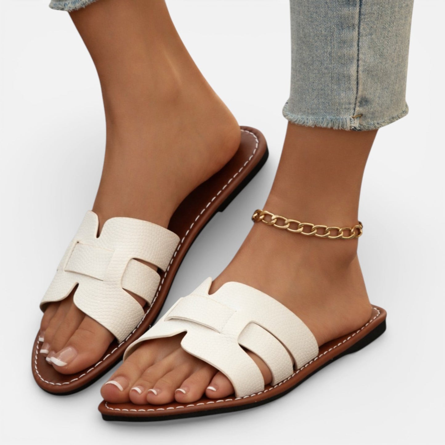 White sandals with brown soles worn by a person on a light gray background