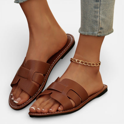 Brown sandals worn with rolled-up jeans on a light gray background