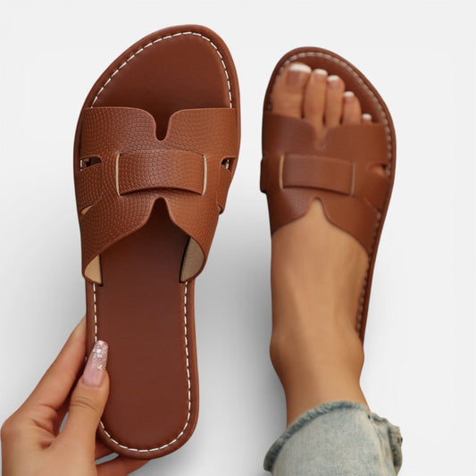 Brown sandals with a bow detail held by a hand on a light gray background