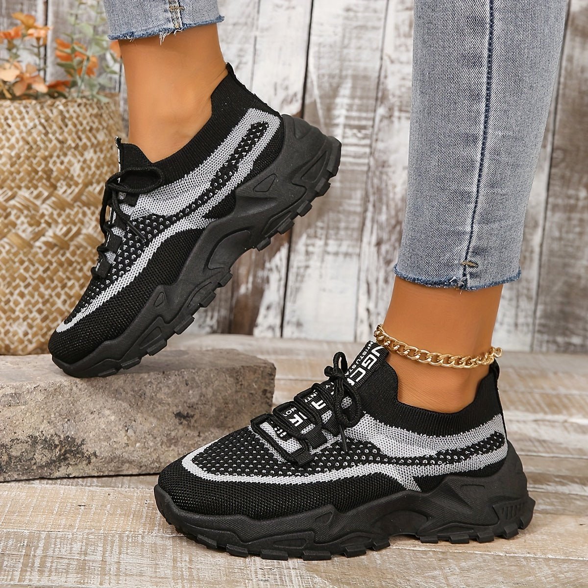 Black and white sneakers worn with light blue jeans on a wooden floor.