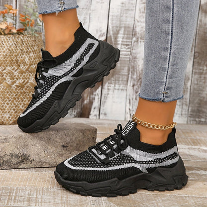 Black and white sneakers worn with light blue jeans on a wooden floor.