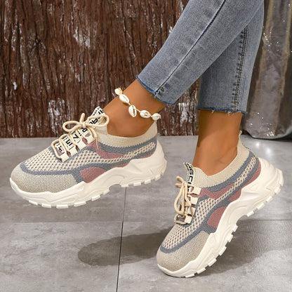 Beige and blue sneakers worn with jeans on a gray floor.