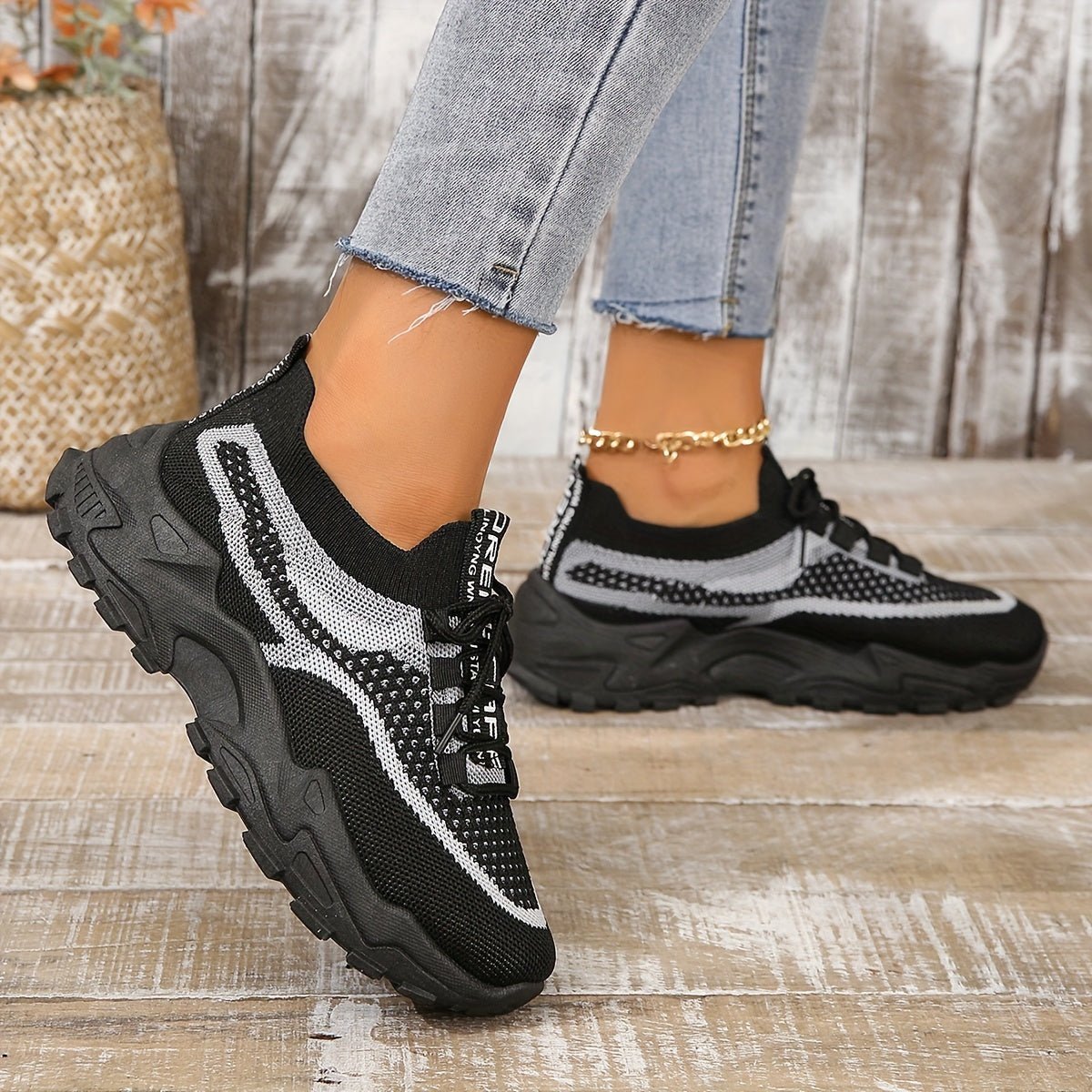 Black and white sneakers worn with light blue jeans on a wooden floor.