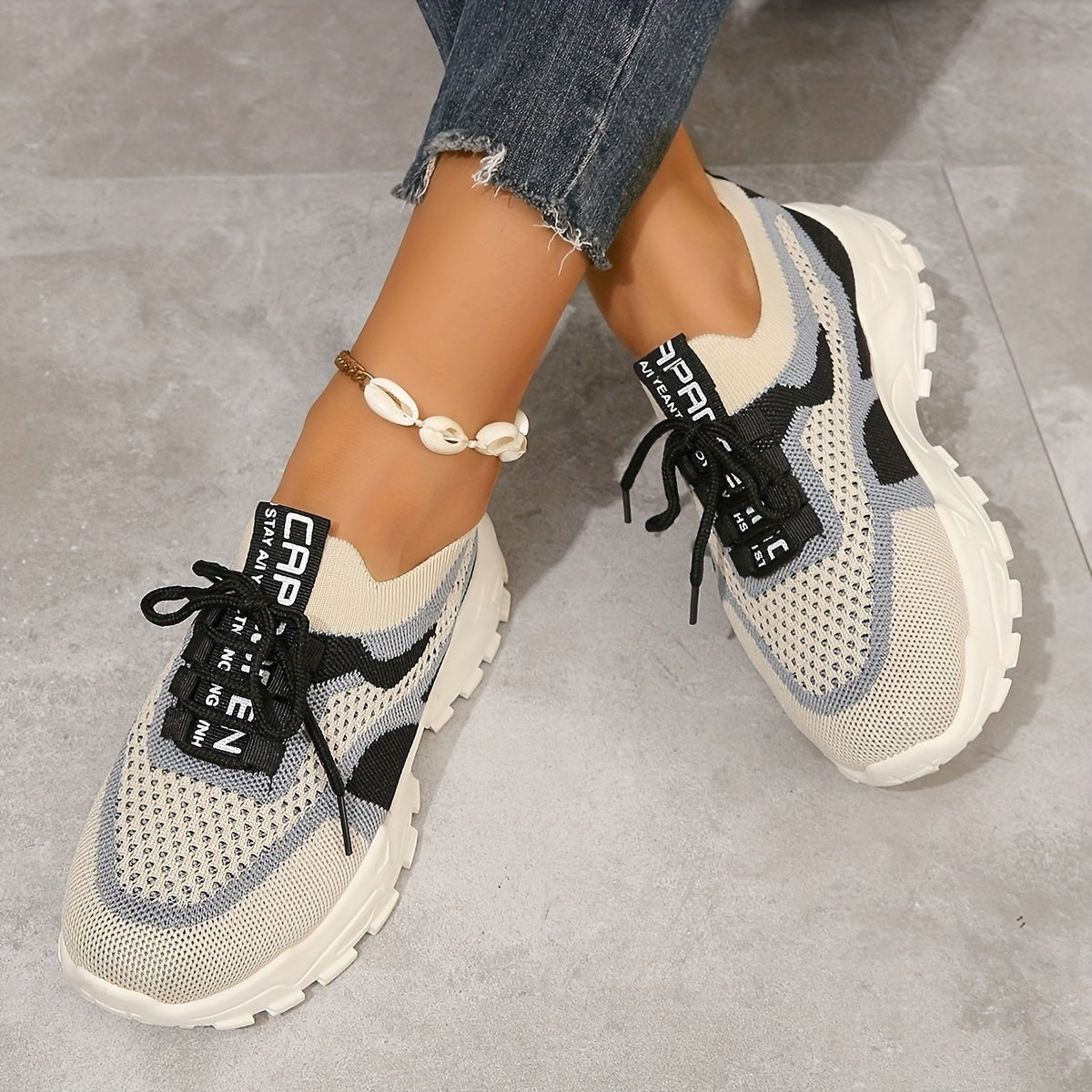 Beige and black sneakers worn with ripped jeans on a gray floor.