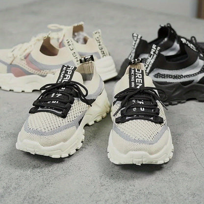 Pair of white sneakers with black laces on a gray surface