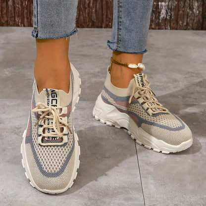 Beige and gray sneakers worn with blue jeans on a concrete floor.