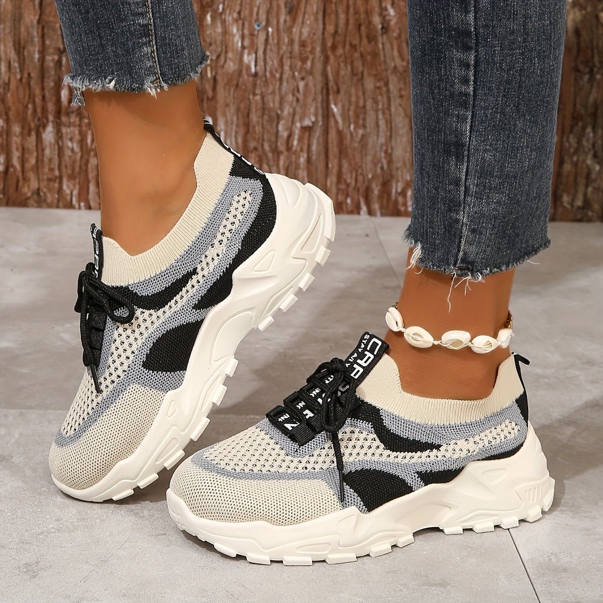 Beige and black sneakers worn with ripped jeans on a neutral background
