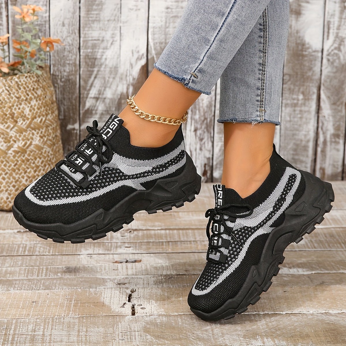Black and white sneakers worn with jeans on a wooden floor.