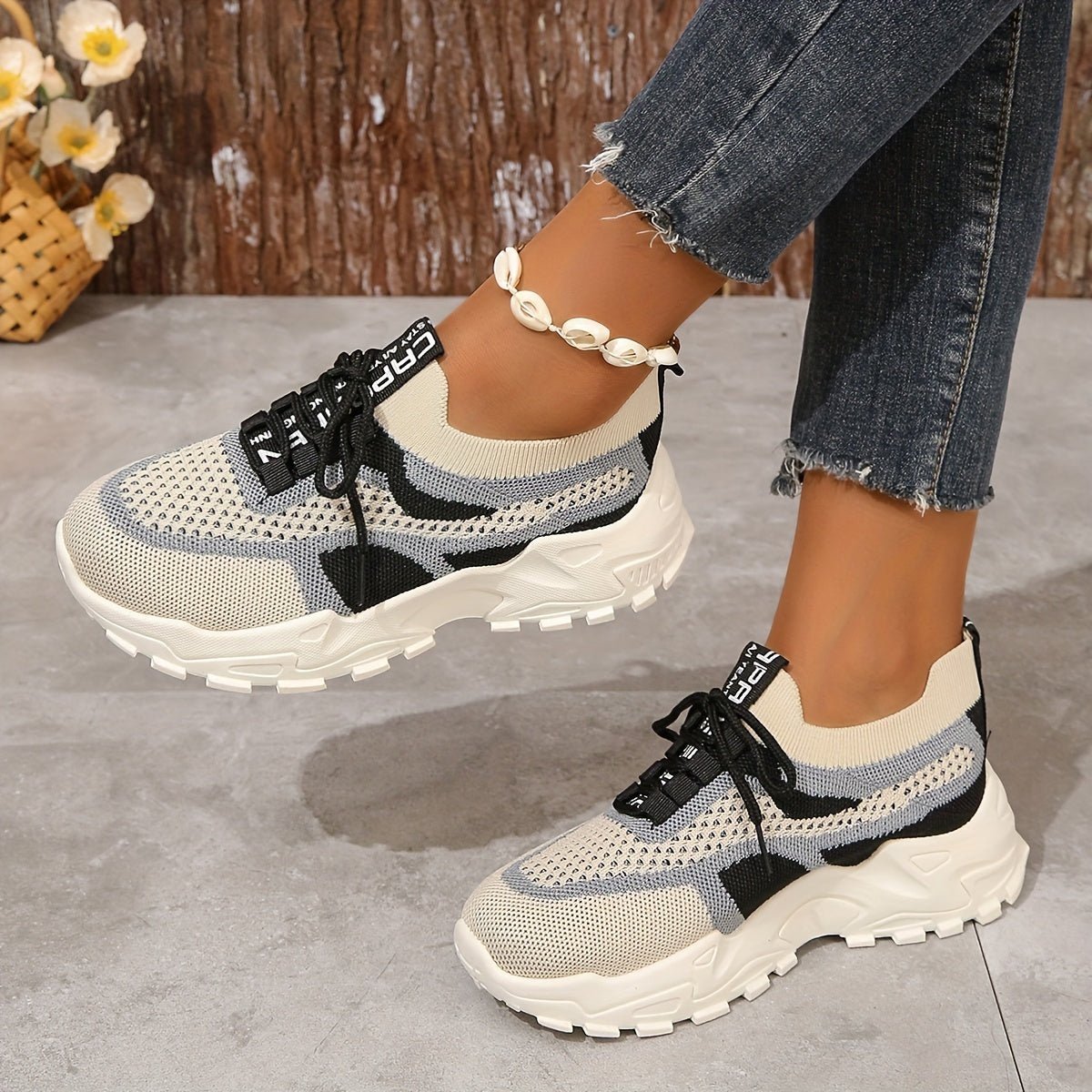 White sneakers with black and gray accents worn by a person on a gray floor.