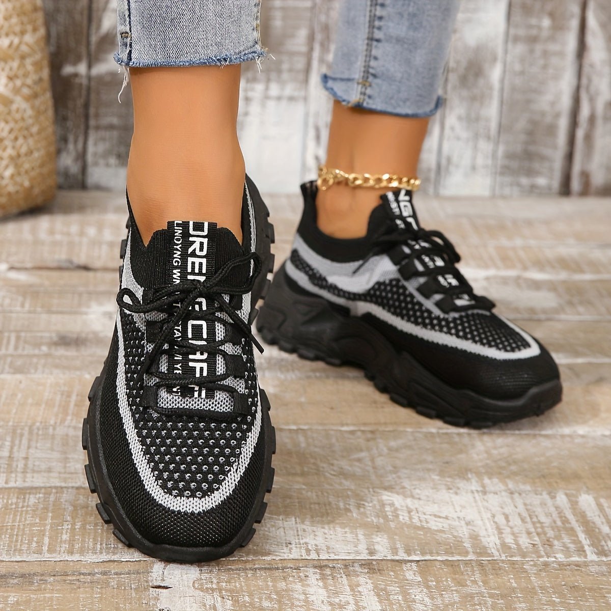Black and white sneakers worn with jeans on a wooden floor.