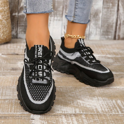 Black and white sneakers worn with jeans on a wooden floor.