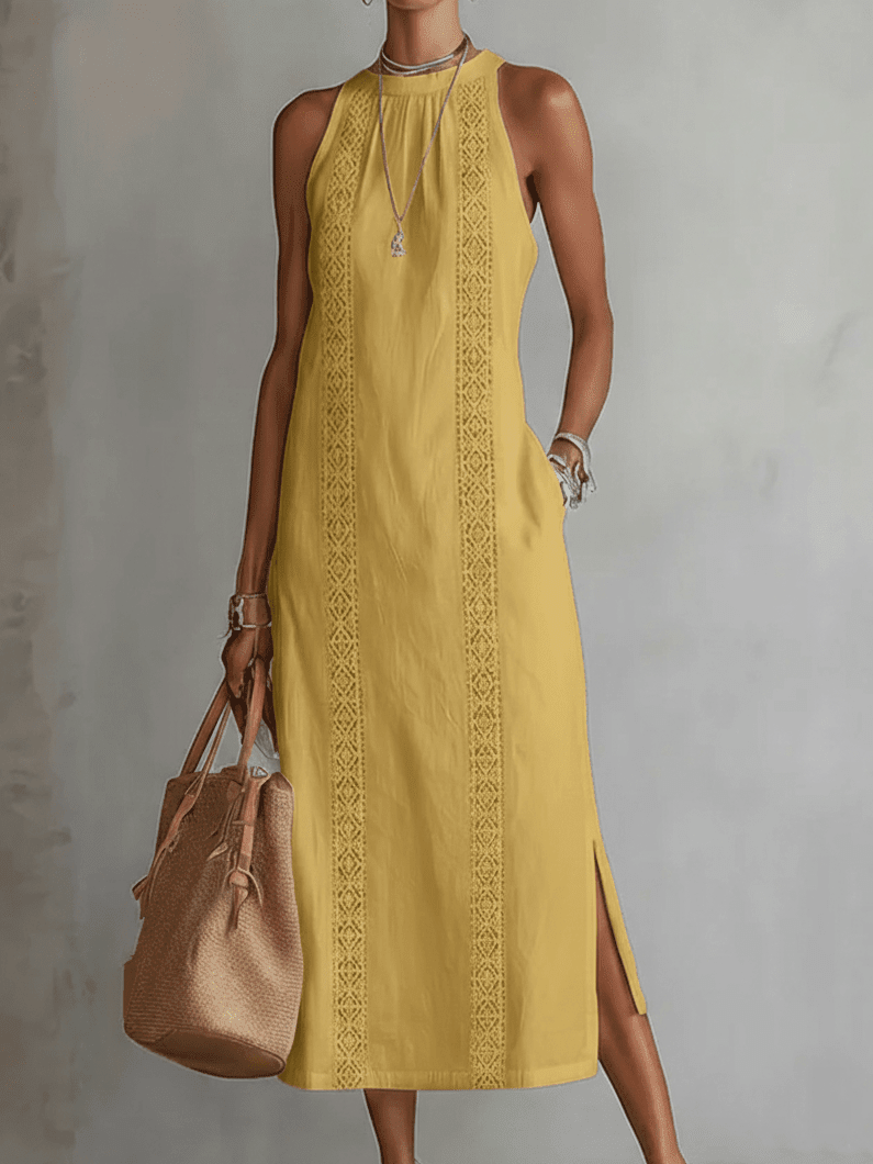 Woman wearing a yellow dress with intricate patterns, holding a brown bag against a gray background