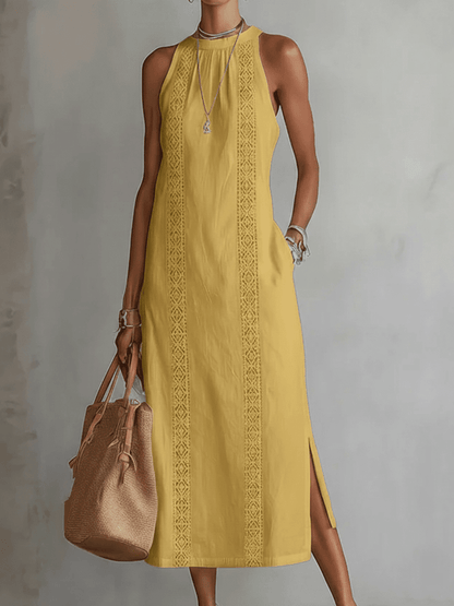 Woman wearing a yellow dress with intricate patterns, holding a brown bag against a gray background