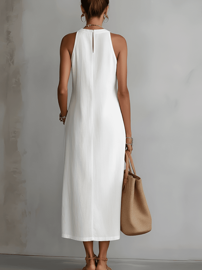 Woman wearing a white sleeveless dress holding a brown handbag against a gray background