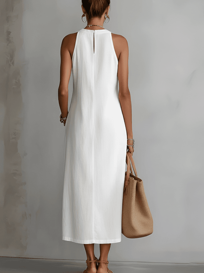 Woman wearing a white sleeveless dress holding a brown handbag against a gray background