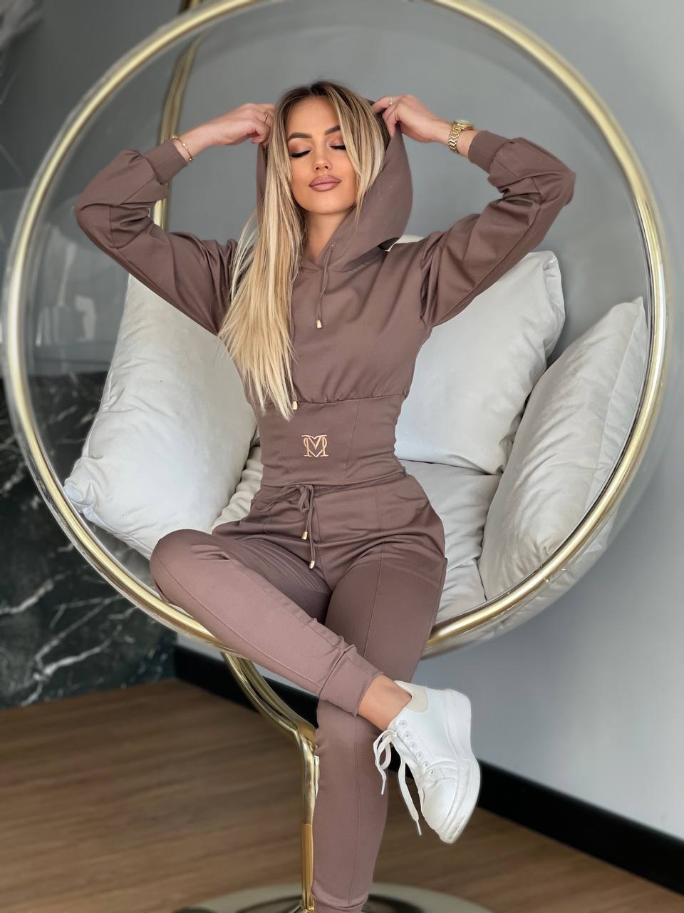 Woman in a brown tracksuit sitting on a modern chair with a neutral background