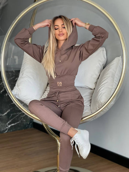 Woman in a brown tracksuit sitting on a modern chair with a neutral background