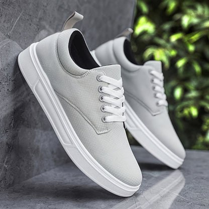 Gray sneakers with white soles leaning against a gray wall with greenery in the background.