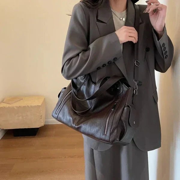 Person wearing a gray suit holding a matching gray bag indoors.