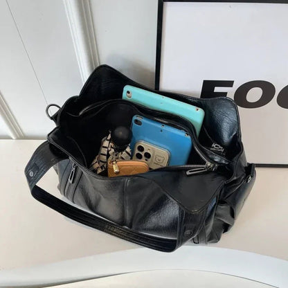 Black leather bag with two smartphones and a wallet on a white surface.