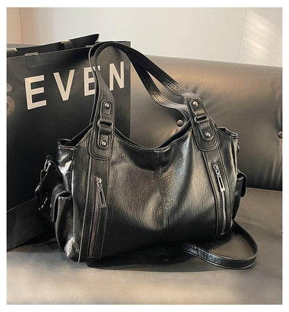 Black leather handbag on a light gray surface with a black background featuring 'EVEN'.