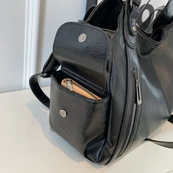 Black leather handbag with a visible pocket on a light surface