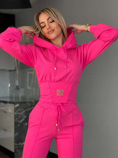 Person wearing a bright pink hoodie and pants with a logo, standing in a modern kitchen.