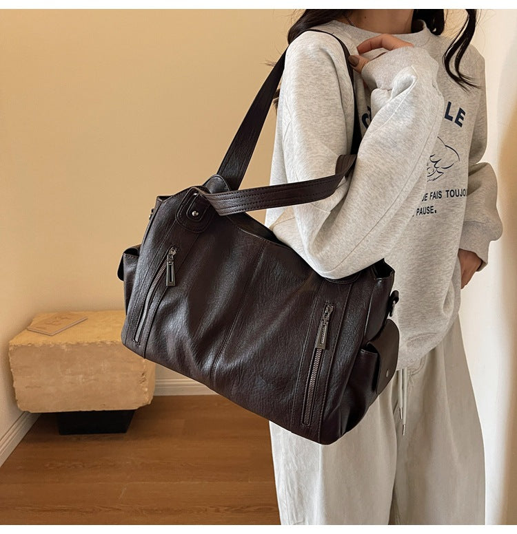Person holding a black leather bag in a room with a wooden floor and beige wall.