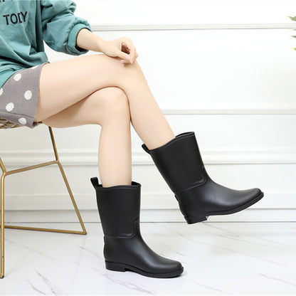 Person wearing black rain boots sitting on a chair with a light background