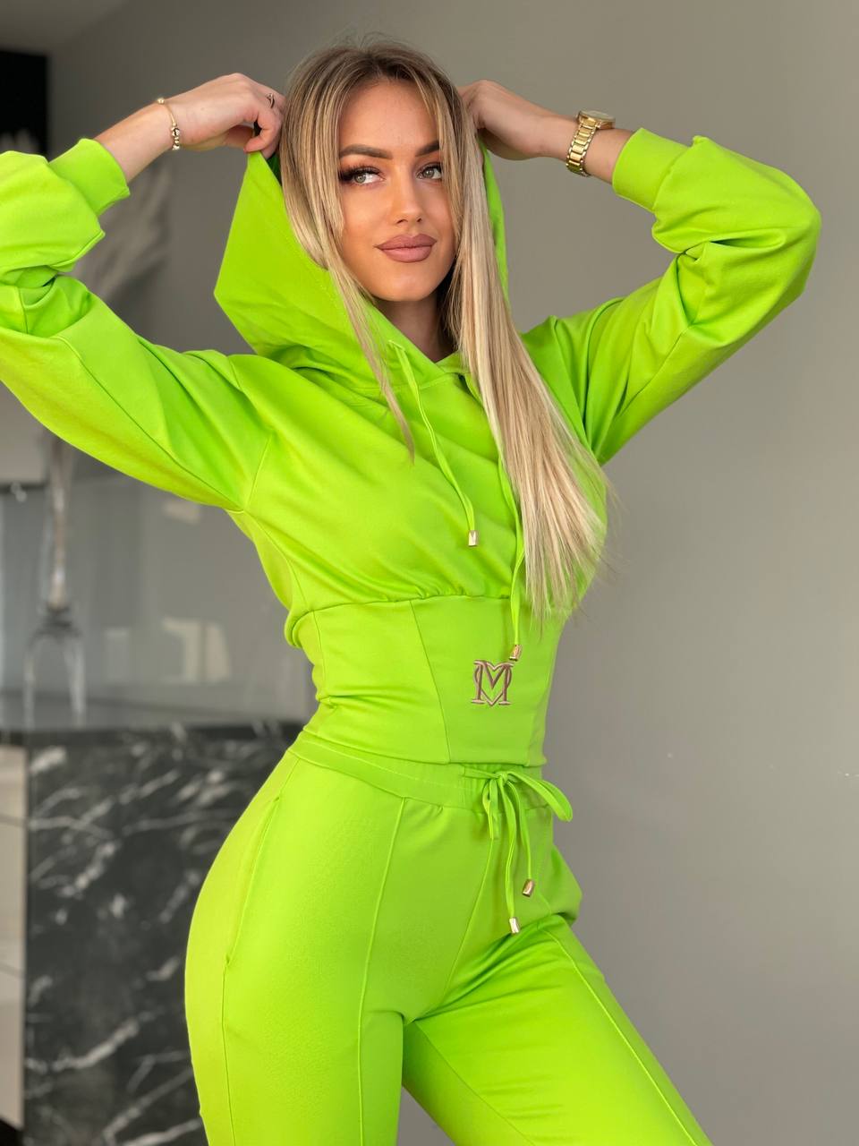 Woman wearing a bright green tracksuit with a logo on a neutral background