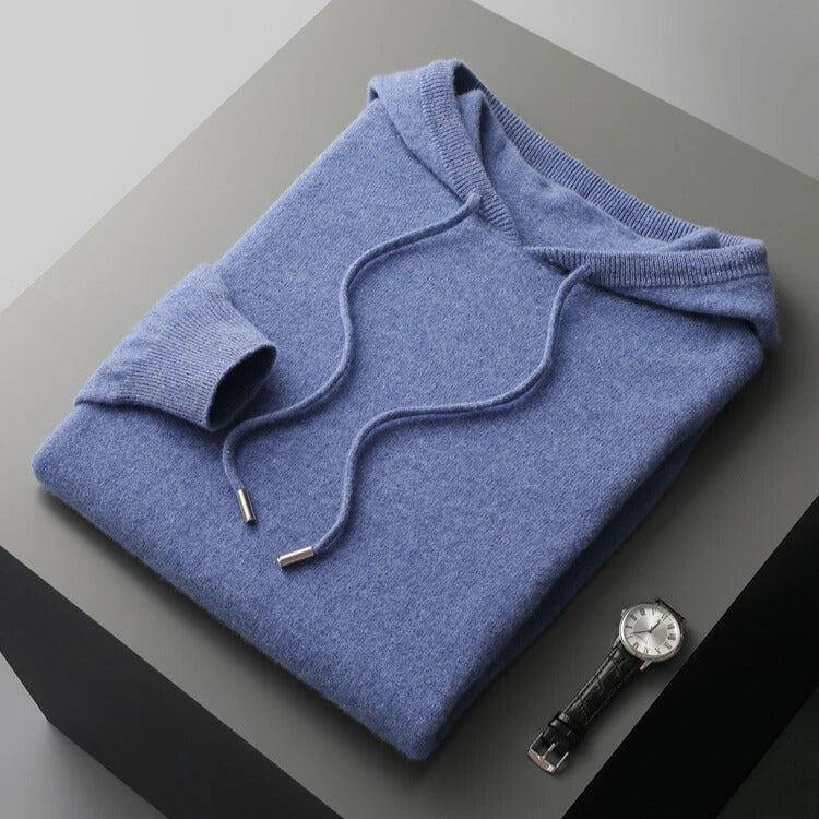 Folded blue hoodie on a gray surface with a watch next to it