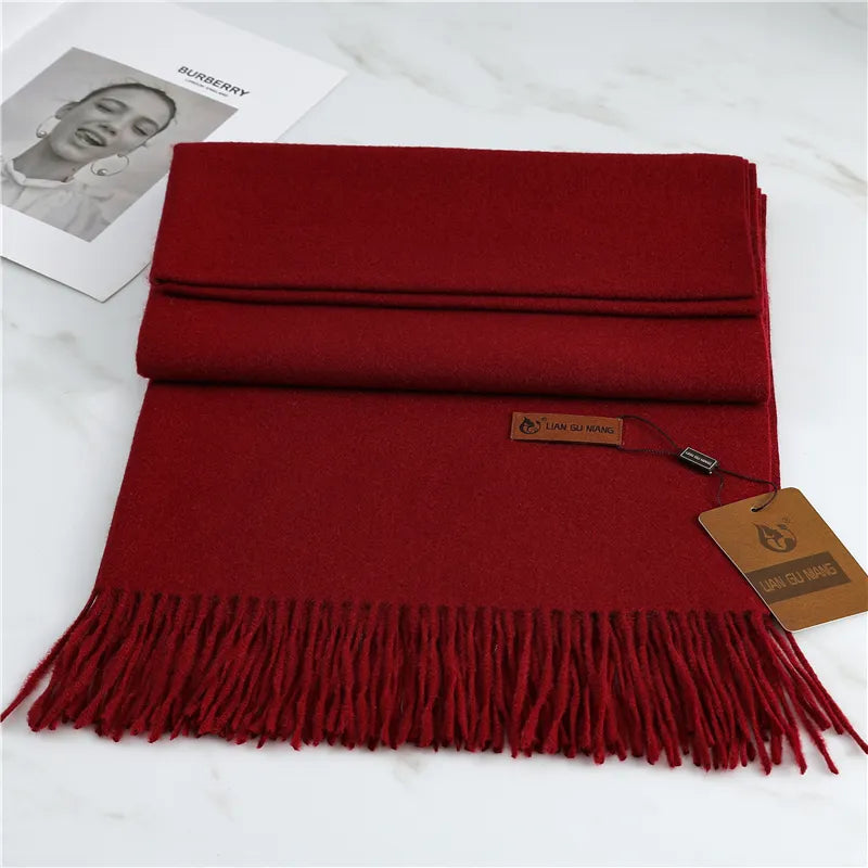 Red scarf with fringes on a white surface, featuring a brand tag.
