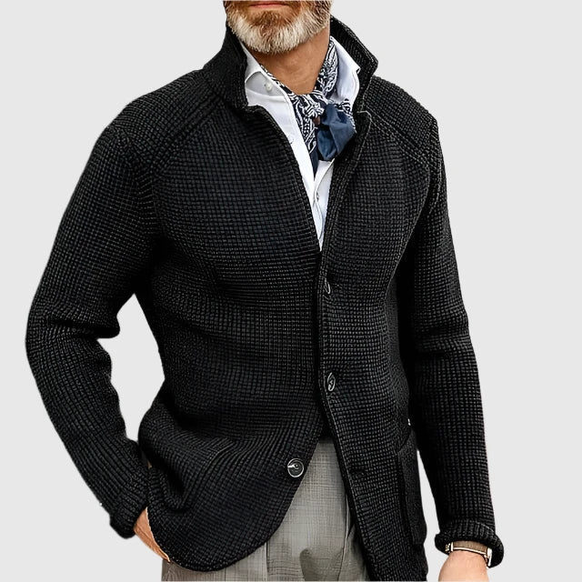 Man wearing a dark textured cardigan over a light shirt with a patterned scarf on a light gray background