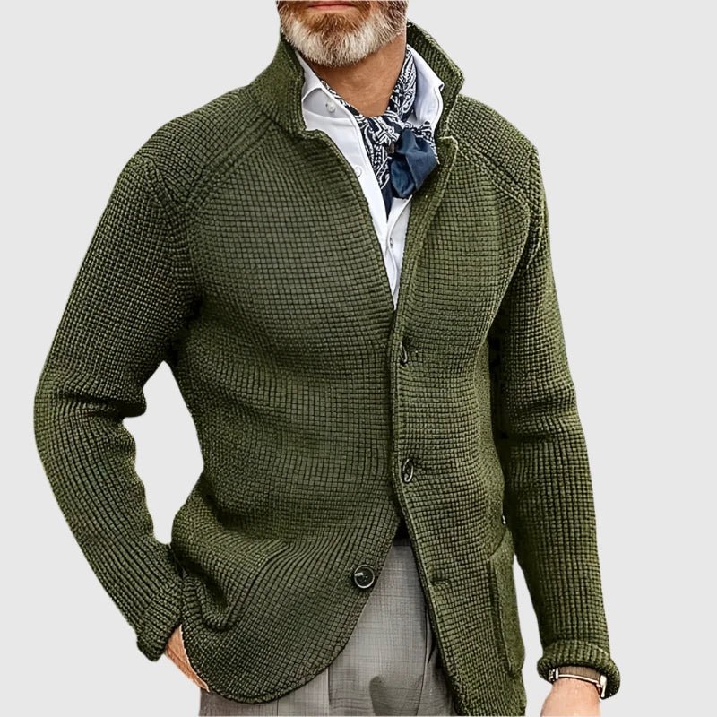 Man wearing a green knitted cardigan over a white shirt with a patterned scarf on a light gray background
