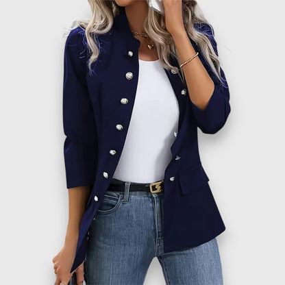 Woman wearing a navy blazer with white buttons, white top, and blue jeans on a light gray background