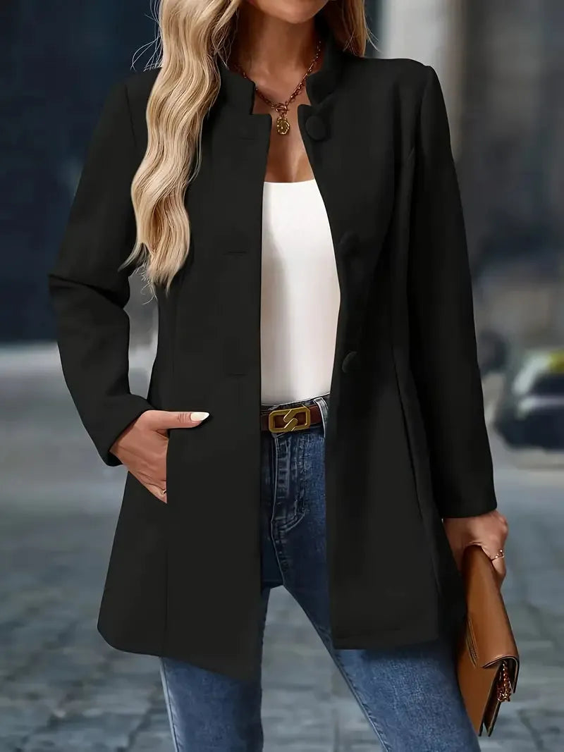 Woman wearing a black coat, white top, blue jeans, and brown handbag on a blurred street background