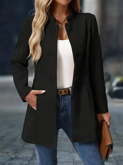 Woman wearing a black coat, white top, blue jeans, and brown handbag on a blurred street background